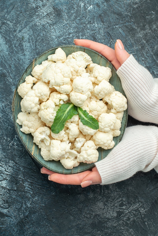 top-view-fresh-cauliflower-inside-plate-female-hands-light-grey-table